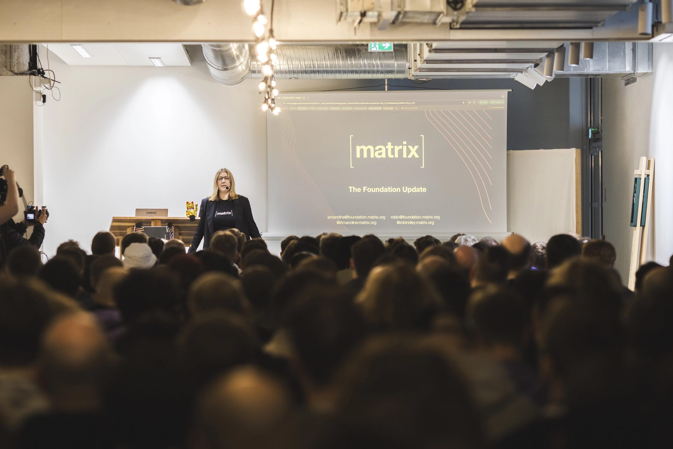 A picture of Amandine, one of the Guardians of The Matrix.org Foundation, standing in front of a large crowd in a packed room. Her slides read 'The Foundation Update'.